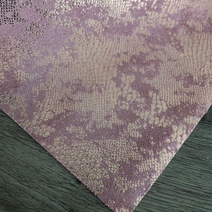 May include: A close-up of a piece of pink fabric with a metallic gold snakeskin pattern.
