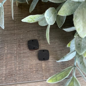 May include: Two square wooden buttons with two holes each. The buttons are dark brown and are on a wooden surface.