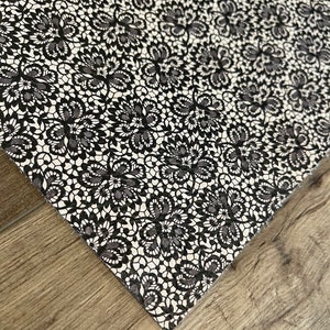 May include: Black and white lace fabric with a delicate floral pattern. The fabric has a smooth texture and a subtle sheen.