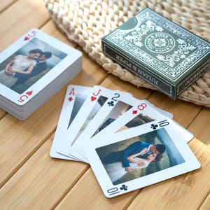 Peut inclure: Un jeu de cartes à jouer personnalisées avec des photographies de mariage sur les faces. L'étui vert foncé affiche le texte Julian & Piper, March 9, 2020, et Our Wedding. Les cartes présentent diverses enseignes, dont un 5 de cœur et un 10 de trèfle.