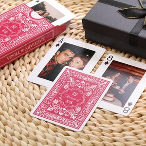 Puede incluir: Una baraja de cartas personalizada con fotos, en una caja roja con el texto "ZACHARY & TESSA" y "52 Moments of US". Las cartas muestran fotos personales y palos de cartas tradicionales.