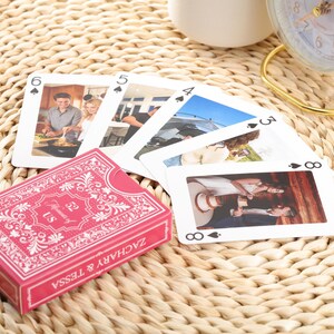 Puede incluir: Una baraja de cartas con una caja rosa con el texto "Moments of US ZACHARY & TESSA". Las cartas muestran fotos y palos de cartas. Las cartas est&aacute;n dispuestas sobre una superficie tejida.