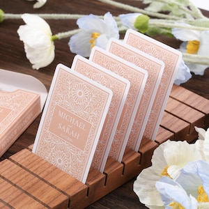 May include: A deck of cards and a matching box with the names "MICHAEL SARAH" printed on them. The cards are displayed in a wooden holder. The cards and box are a light peach color with a floral design.
