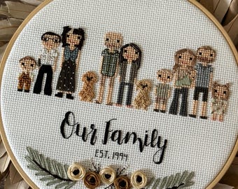 May include: A circular wooden embroidery hoop containing a cross-stitch design on white fabric. The design features stylized figures of adults, children, and small dogs, with the text "Our family" and "EST. 1994" above embroidered floral accents.