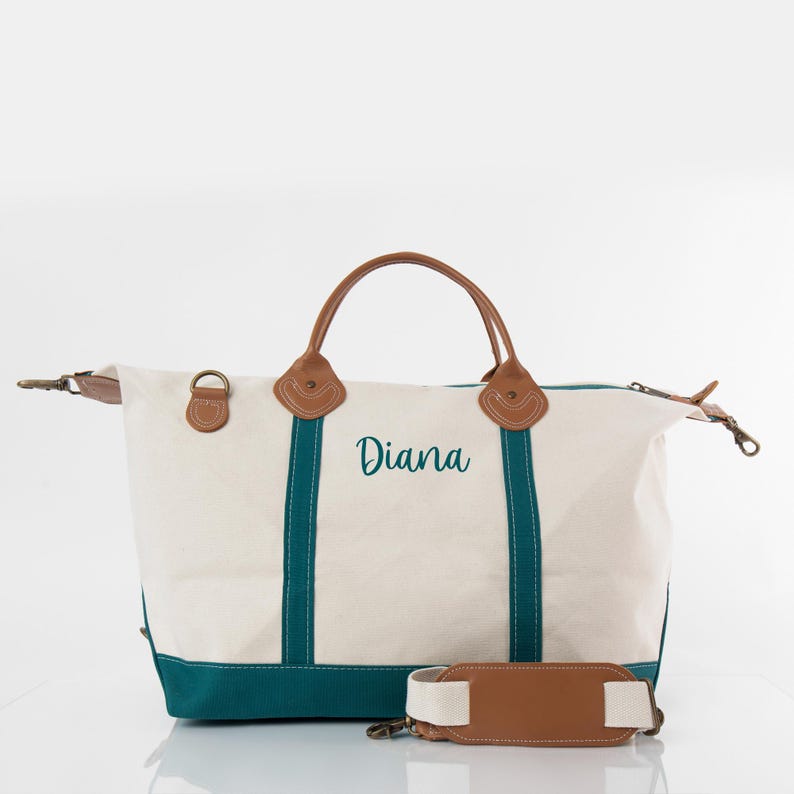 May include: Cream-colored canvas tote bag with teal accents and brown leather handles and trim. The name "Diana" is embroidered in teal script on the front. Includes a detachable shoulder strap.