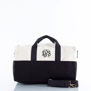 May include: A white and black canvas duffel bag with a black monogrammed initial "S" on the front. The bag has a black shoulder strap and a zipper closure.