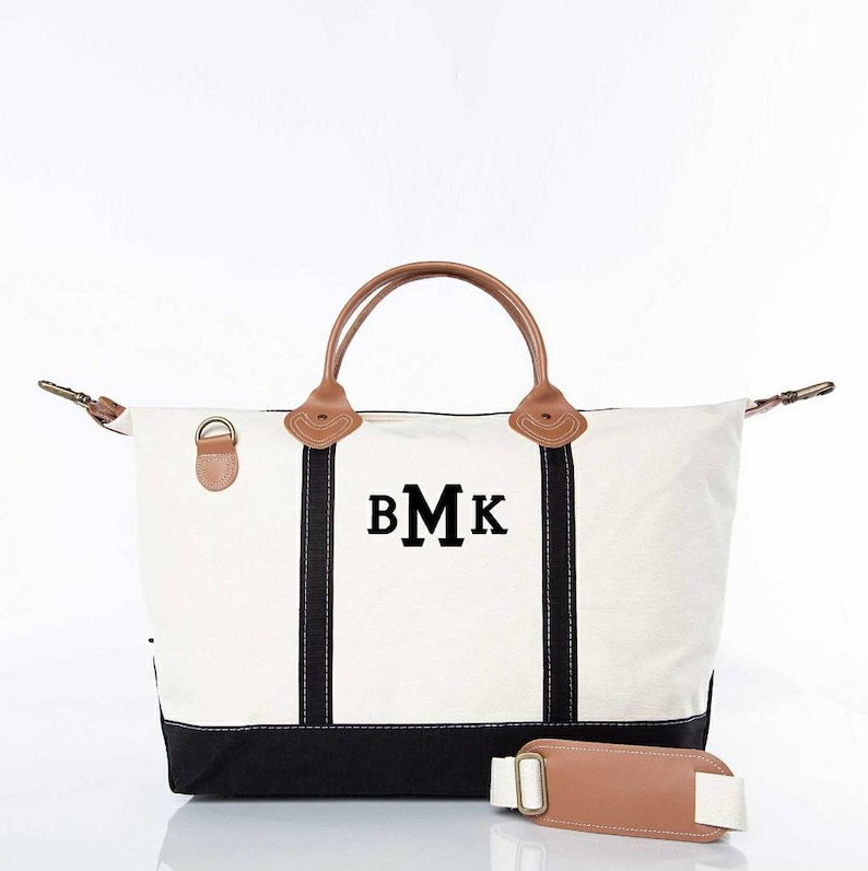 May include: Cream-colored canvas tote bag with black accents and brown leather handles. The bag features the initials "BMK" in black block letters. Includes a detachable shoulder strap with a brown leather pad.
