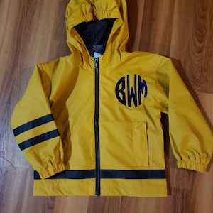 May include: A yellow hooded jacket with black stripes on the sleeves and a black band around the bottom. The jacket has a zipper closure and a black circle with the letters "BWM" embroidered on the front.
