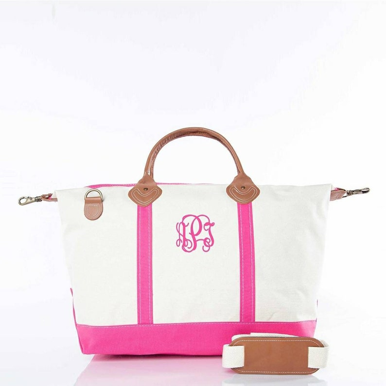 May include: White canvas tote bag with a hot pink base and vertical stripes. Features brown leather handles and accents, a detachable shoulder strap, and a monogram in the center. The bag has a classic, preppy style.