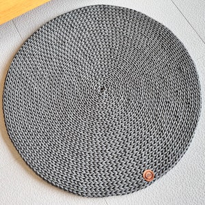 May include: A round, gray, crocheted rug with a brown leather tag in the lower right corner.