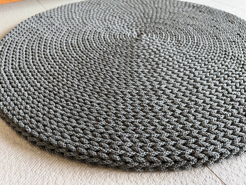 May include: A round gray braided rug with a textured surface.