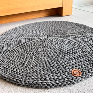 May include: A gray round crocheted rug with a brown button in the center.