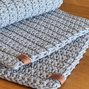 Pode incluir: Uma manta de crochê cinza com uma etiqueta de couro marrom que diz "Blue Handmade".