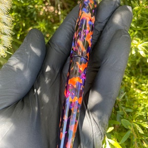 Puede incluir: Una pluma estilogr&aacute;fica con un patr&oacute;n morado, naranja y negro.