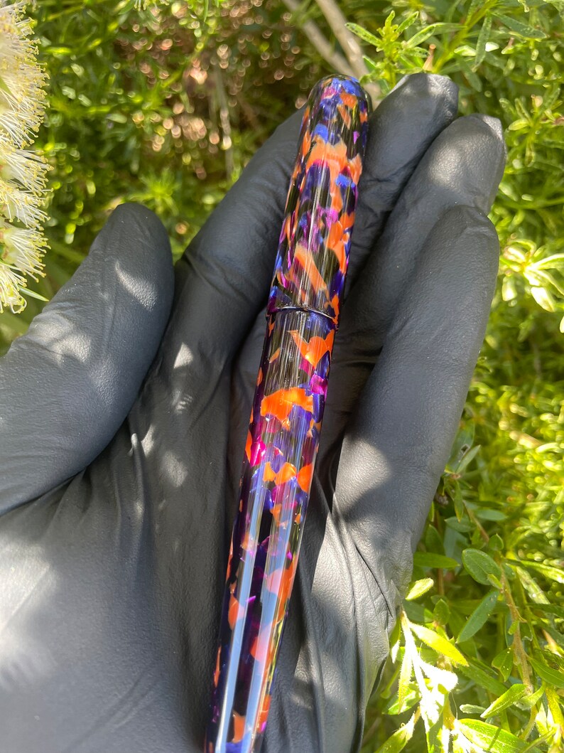 Puede incluir: Una pluma estilogr&aacute;fica con un patr&oacute;n morado, naranja y negro.