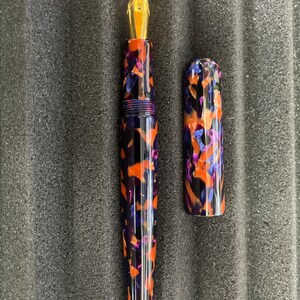 Puede incluir: Una pluma estilogr&aacute;fica negra y naranja con una punta de oro y un capuch&oacute;n a juego. La pluma tiene un patr&oacute;n de m&aacute;rmol.