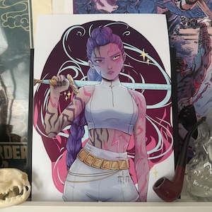 Può includere: Stampa con illustrazione stilizzata di una figura femminile con capelli viola, che tiene una spada. La figura indossa un top e pantaloni bianchi con una cintura dorata. Lo sfondo è viola scuro con accenti rosa.
