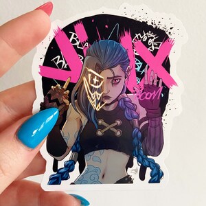 May include: A sticker featuring a cartoon illustration of a female character with blue hair and a gold mask. The character is wearing a black tank top with a white cross on it and a black and white bandana. The background is black with pink and white graffiti. The text "BOOM" is written in white on the sticker.