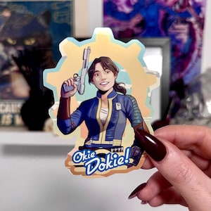 Può includere: Un adesivo con un personaggio sorridente che tiene in mano una pistola, su uno sfondo a forma di ingranaggio con una sfumatura giallo chiaro e blu. L'adesivo riporta la scritta "Okie Dokie!" in un font stilizzato.