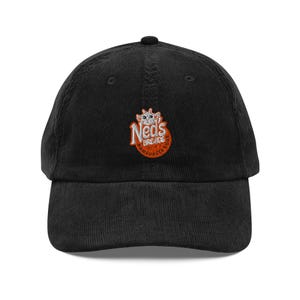 Op de afbeelding: Zwarte corduroy baseballcap met de geborduurde tekst "Neds Breads Hamburger Buns" in oranje en wit. De cap heeft een gebogen klep en een knoop aan de bovenkant.