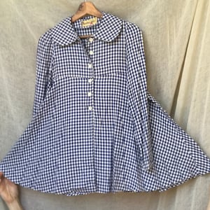 May include: A blue and white gingham button-up shirt with a Peter Pan collar and long sleeves. The shirt has a flared hem and is made of a lightweight fabric.