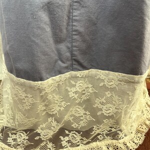 May include: A close-up of a blue fabric with a white lace trim. The lace features a floral pattern and a scalloped edge. The fabric appears to be a dress or a garment.