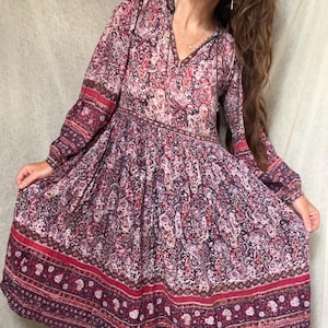 Könnte beinhalten: Langärmliges Kleid mit Paisley-Muster in Burgunder-, Rosa- und Lilatönen. Das Kleid hat einen V-Ausschnitt, eine geraffte Taille und einen breiten Saum. Die Ärmel sind lang und das Kleid hat eine fließende Silhouette.