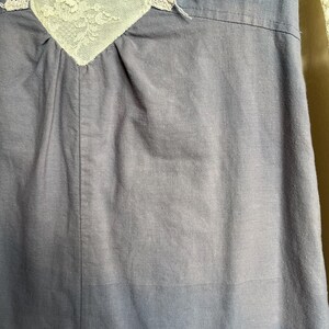 May include: Close-up of a blue dress with a white lace detail at the neckline. The lace is intricately designed with floral patterns. The dress has a simple, classic design.