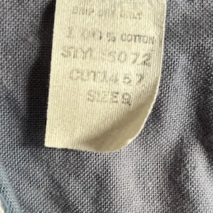 May include: Close-up of a fabric tag with text. The tag is cream-colored and attached to a blue fabric. The tag reads "100% COTTON", "STY 5072", "CUT 1457", and "SIZE 9".
