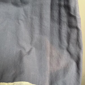 May include: Close-up of a section of fabric. The main part is a muted blue-gray color, with a lighter, off-white lace trim at the bottom. The fabric has a slightly textured appearance.