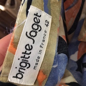 May include: A close-up of a garment with a colorful floral pattern in shades of blue, orange, and beige. A white tag reads "brigitte joget" and "made in France 42".