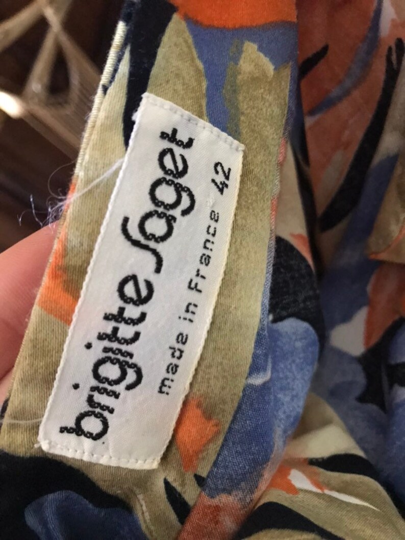 May include: A close-up of a garment with a colorful floral pattern in shades of blue, orange, and beige. A white tag reads "brigitte joget" and "made in France 42".