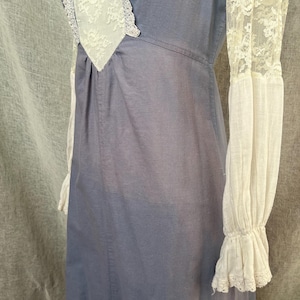 May include: A blue dress with white lace trim and sleeves. The dress has a high neckline with a white lace insert. The long sleeves are white with lace detailing at the cuffs. The dress appears to be made of a soft, lightweight fabric.