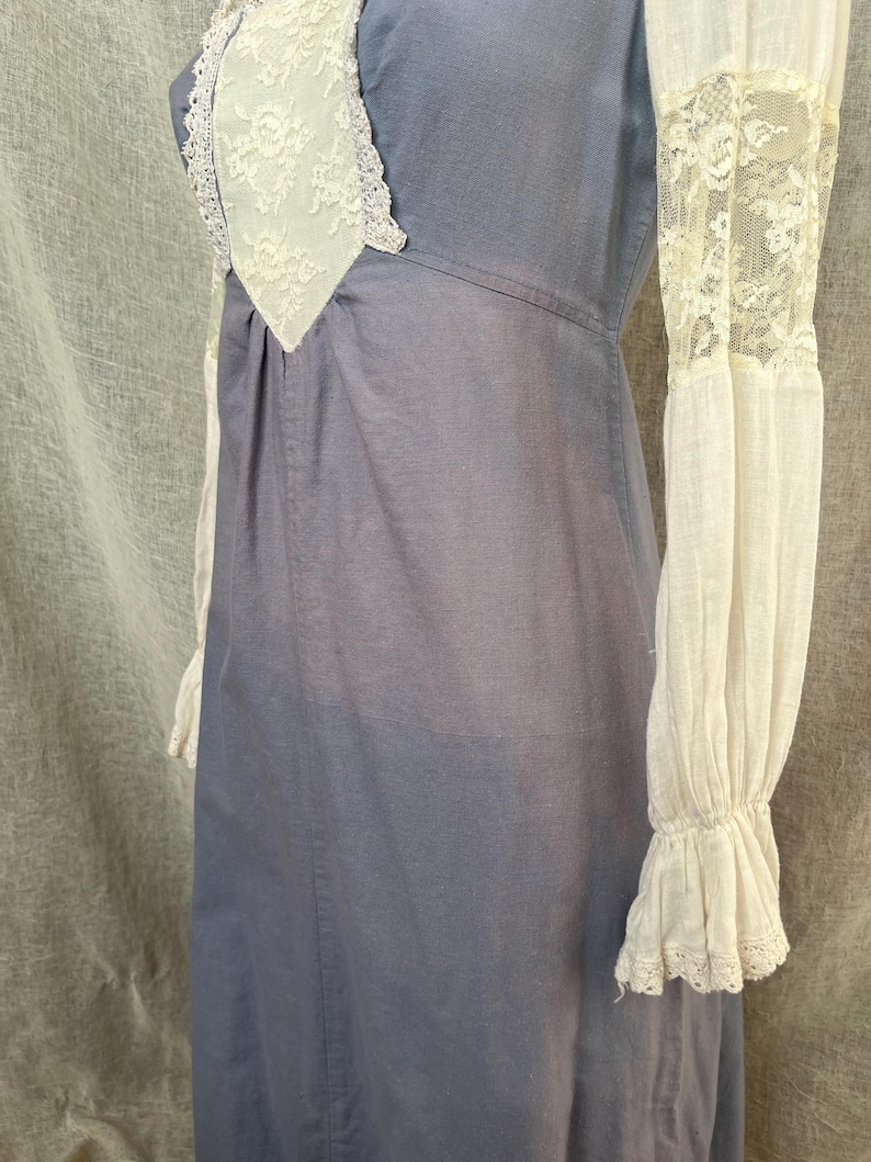 May include: A blue dress with white lace trim and sleeves. The dress has a high neckline with a white lace insert. The long sleeves are white with lace detailing at the cuffs. The dress appears to be made of a soft, lightweight fabric.