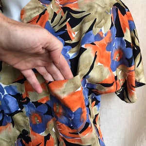 May include: A button-down shirt with a vibrant floral pattern in orange, blue, black, and tan. The shirt features a chest pocket and short sleeves. The fabric appears to be lightweight.