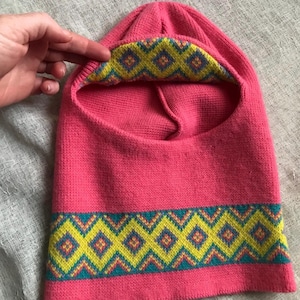 Puede incluir: Balaclava de punto rosa con un patrón geométrico amarillo y azul alrededor del borde inferior.