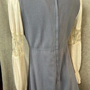 May include: A vintage-style dress featuring a light blue bodice and cream-colored sleeves. The sleeves have lace detailing at the cuffs. The dress has a high neckline and a vertical seam down the back.