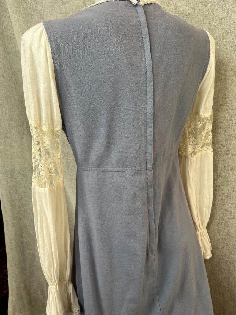May include: A vintage-style dress featuring a light blue bodice and cream-colored sleeves. The sleeves have lace detailing at the cuffs. The dress has a high neckline and a vertical seam down the back.