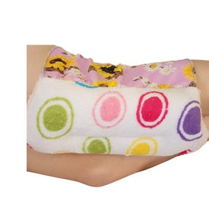 May include: A white, fluffy elbow pad with colourful circles. The pad is made of soft, plush fabric and is designed to protect the elbow from pressure and friction.