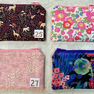 Op de afbeelding: Vier kleine etuis met ritssluiting met verschillende bloemen- en natuurpatronen. E&eacute;n etui heeft een zwarte achtergrond met bosdieren, een andere heeft roze bloemen, een derde heeft roze en witte bloemen en de laatste heeft een donkerblauw bloemmotief.
