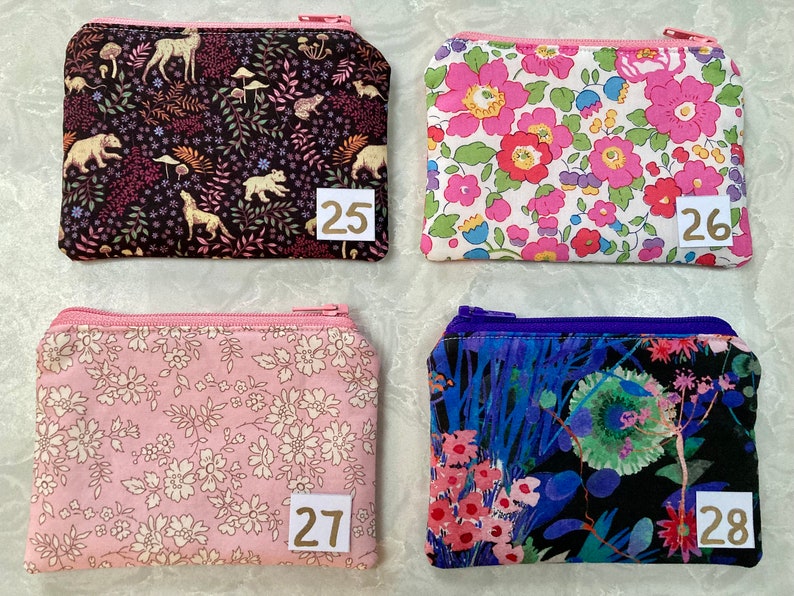 Op de afbeelding: Vier kleine etuis met ritssluiting met verschillende bloemen- en natuurpatronen. E&eacute;n etui heeft een zwarte achtergrond met bosdieren, een andere heeft roze bloemen, een derde heeft roze en witte bloemen en de laatste heeft een donkerblauw bloemmotief.