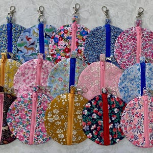 以下が含まれることがあります： さまざまな花柄と模様の生地で作られた、丸いジッパー付きポーチが13個セットです。ポーチはすべて直径約10cmで、青いジッパーまたは赤いジッパーが付いています。