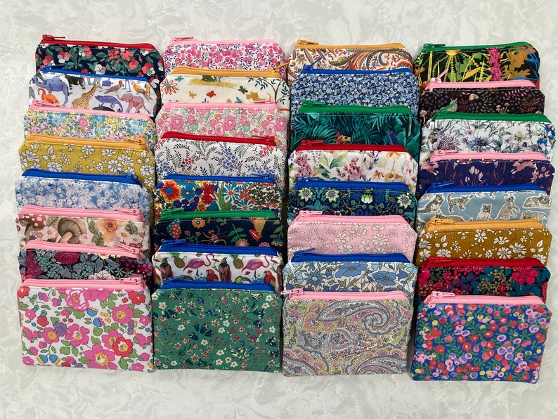 Op de afbeelding: Een verzameling kleine, rechthoekige etuis met ritssluiting in diverse bloemen- en patroonstoffen. De etuis hebben een reeks kleuren, waaronder roze, blauw, groen en geel, met contrasterende ritssluitingkleuren.
