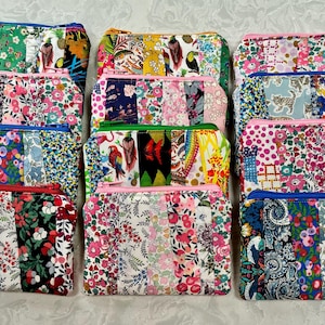 Può includere: Una collezione di pochette con cerniera in tessuto patchwork colorato. Le pochette presentano disegni floreali e fantasia in vari colori, tra cui rosa, blu, verde e giallo. Ogni pochette ha una cerniera a contrasto.