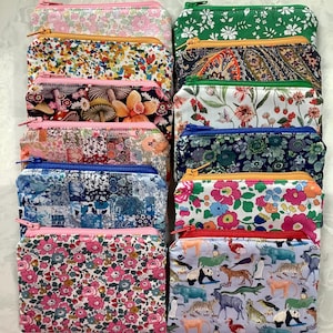 May include: A selection of zippered pouches with diverse floral and animal prints. The pouches have different coloured zippers, including pink, orange, and red. The fabrics display a range of colours, including pink, green, blue, and white.