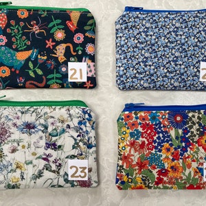 Op de afbeelding: Vier kleine, rechthoekige etuis met ritssluiting en verschillende bloemen- en patroonstoffen. De etuis hebben een verscheidenheid aan kleuren, waaronder blauw, groen, rood en wit. Elk etui heeft een klein, genummerd label. De etuis zijn waarschijnlijk voor het dragen van kleine items.