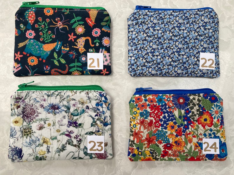 Op de afbeelding: Vier kleine, rechthoekige etuis met ritssluiting en verschillende bloemen- en patroonstoffen. De etuis hebben een verscheidenheid aan kleuren, waaronder blauw, groen, rood en wit. Elk etui heeft een klein, genummerd label. De etuis zijn waarschijnlijk voor het dragen van kleine items.