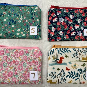 Op de afbeelding: Vier kleine, rechthoekige etuis met ritssluiting en bloemen- en natuurelementen. De etuis hebben verschillende gekleurde ritsen en zijn genummerd 5, 6, 7 en 8. De patronen omvatten bloemen, honden en bladeren.
