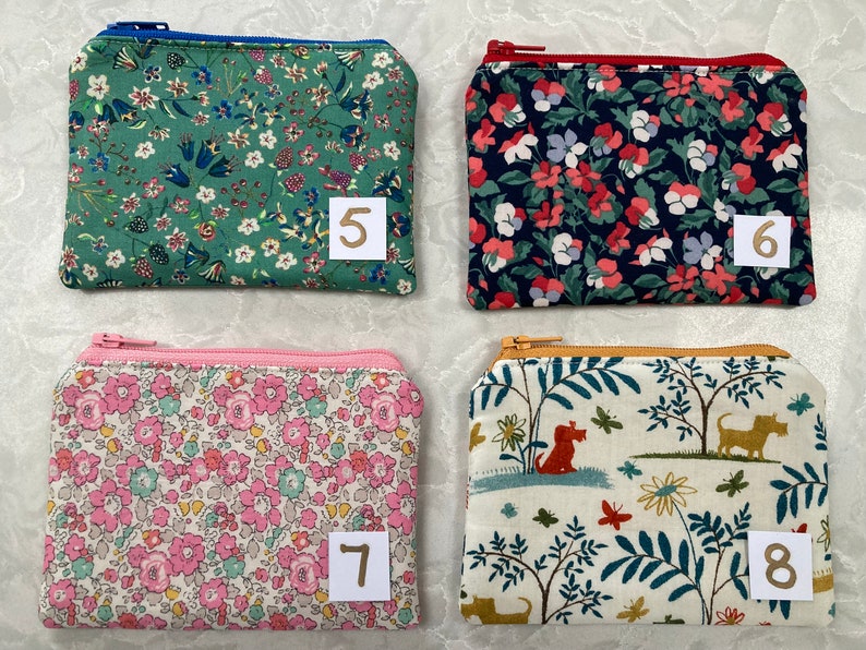 Op de afbeelding: Vier kleine, rechthoekige etuis met ritssluiting en bloemen- en natuurelementen. De etuis hebben verschillende gekleurde ritsen en zijn genummerd 5, 6, 7 en 8. De patronen omvatten bloemen, honden en bladeren.