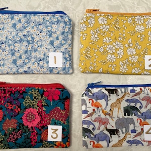 Op de afbeelding: Vier kleine etuis met ritssluiting met verschillende bloemen- en dierenpatronen. De etuis zijn rechthoekig en hebben een ritssluiting. De eerste is lichtblauw met witte bloemen. De tweede is geel met witte bloemen. De derde is rood met bloemen. De vierde is wit met dieren.